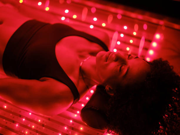 A multiracial woman on an LED light bed, receiving red light therapy.